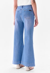 Lichtblauwe wijde denim jeans met een hoge taille, voorzien van achterzakken en knoopdetails op de zijnaad. Gladde textuur, casual ontwerp.