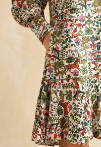 Kleid mit Blumenmuster in lebhaften Farben, darunter Grün, Rot und Blau, mit einem gerafften Rock und Taschen für zusätzliche Details.