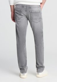 Jeans di denim grigio con silhouette a gamba dritta, dotati di due tasche posteriori e dettagli di texture sottili. Indossati con sneakers bianche.