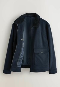 Tummansininen bleiseri fleece-kauluksella, etuvetoketju osittain avoinna, ja napilliset läppätaskut molemmilla puolilla.