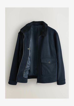 Ciemnogranatowa kurtka z kołnierzem z polaru, częściowo rozpiętym przednim suwakiem i kieszeniami na klapki zapinanymi na guziki po obu stronach.