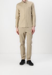 Beige overhemd met lange mouwen, gecombineerd met bijpassende beige broek. Zwarte sneakers maken de outfit compleet. Eenvoudig, casual ontwerp.