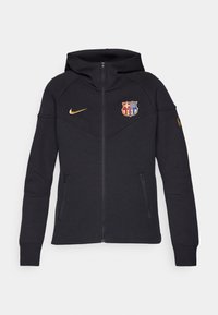 Sweat à capuche zippé noir avec un logo Nike doré sur la poitrine droite et un blason coloré du FC Barcelone sur la poitrine gauche.