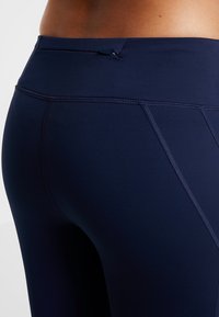 Granatowe leggings sportowe o gładkiej fakturze, z płaskimi szwami i małą, bezpieczną kieszonką na zamek w talii.