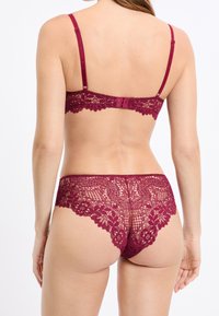 Completo intimo bordeaux in pizzo con motivi floreali, spalline regolabili, chiusura a ganci e bordi smerlati per un design delicato.