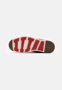 Suela de zapato con un patrón de olas y acentos rojos, goma beige y una sección marrón. Logo de "Levi's" visible en la suela.