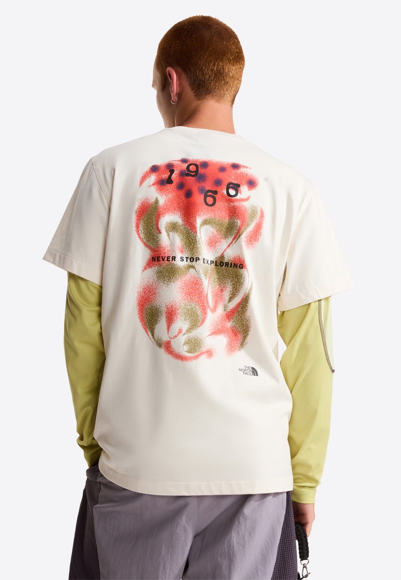 Helles cremefarbenes T-Shirt mit kurzen Ärmeln und einem bunten abstrakten Design auf der Rückseite, das den Text "1966" und "NEVER STOP EXPLORING" enthält.