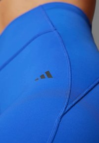 Modré športové legíny z hladkej látky s čiernym logom a kontrastným šitím, s priliehavým, tvarovaným strihom.