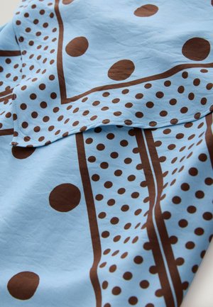 Close-up of light blue fabric with brown polka dots and rectangular border patterns, showing layered folds and visible stitching.