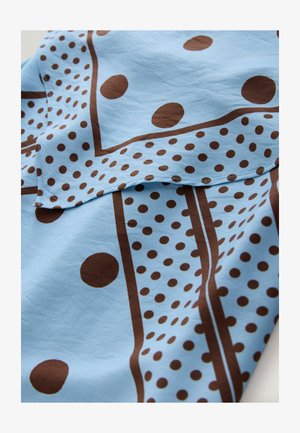 Close-up of light blue fabric with brown polka dots and rectangular border patterns, showing layered folds and visible stitching.
