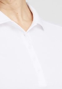 Närbild av en person som bär en vit skjorta med krage med fyra knappar knäppta, som visar nacke och övre bröstområde.