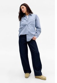 Gaiši zils, svītrains krekls ar garām piedurknēm un pogu aizdari, kombinēts ar plašām tumši zilām džinsu biksēm un bēšām slip-on kurpēm. Vienkāršs dizains, brīvs piegriezums.