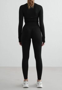 Haut à manches longues noir et leggings en tissu extensible. Coupe ajustée avec un design sans coutures et des accents minimalistes. Baskets blanches incluses.