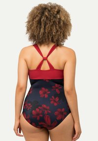 Maillot de bain une pièce rouge et marine avec un motif floral. Il présente des bretelles croisées réglables et un corps solide rouge en haut.