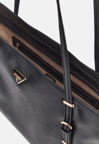 Borsa a tracolla in pelle nera con superficie strutturata, dettagli in ottone dorato e diversi scomparti, inclusa una tasca con zip e due manici.