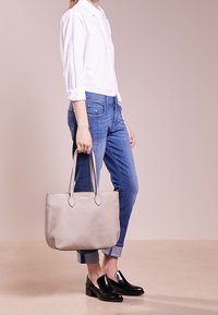 Sac fourre-tout gris avec poignées doubles, texture en cuir lisse et forme ovale. Assorti à un jean bleu et des mocassins noirs. Design simple.