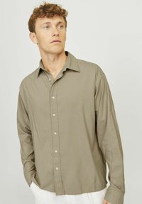 Camisa de manga larga verde oliva claro en tejido ligero con cierre frontal de botones, cuello clásico y corte relajado, que presenta una sutil textura.