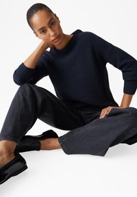 Maglione a maglia blu navy con texture a coste, colletto rotondo e polsini lunghi, abbinato a jeans larghi in denim scuro e scarpe flat nere.