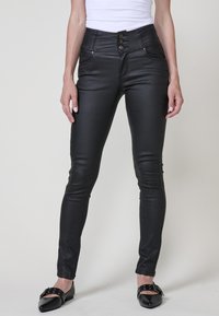 Pantalones skinny de imitación cuero negros con cintura alta, cierre de tres botones y bolsillos frontales. Textura suave y diseño elegante.