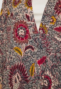 Tkanina w kwiatowy wzór z czerwonymi, żółtymi i białymi kwiatami oraz czarnymi, spiralnymi detalami na białym prążkowanym topie.