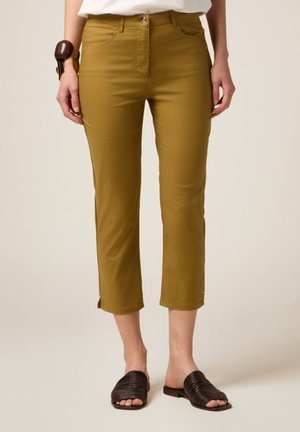 Pantalons cropped couleur olive avec une texture lisse, poches avant et détails zippés à l'ourlet. Associés à des sandales tressées marron.
