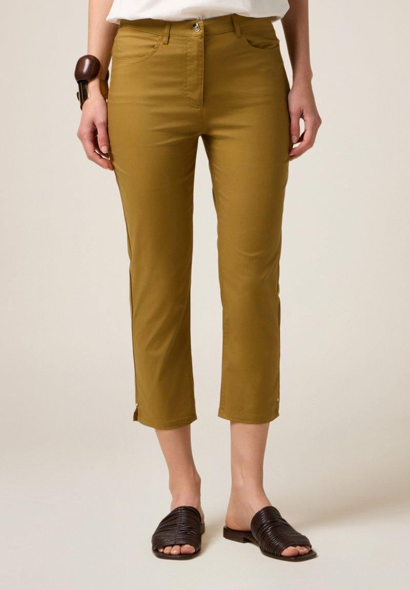 Olijfgroene cropped broek met een gladde textuur, voorzakken en ritsaccenten aan de onderkant. Gepaard met bruine gevlochten sandalen.