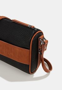 Czarna torebka skórzana o teksturowanej powierzchni z brązowym skórzanym paskiem i akcentami. Posiada zamek błyskawiczny oraz wytłoczone logo z przodu.