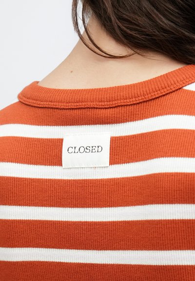 Πουκάμισο ριγωτό σε σκουριά-πορτοκαλί και λευκό, πλεκτό με ραβδώσεις, με στρογγυλή λαιμόκοψη και ορατή ετικέτα με την ένδειξη "CLOSED" στην πλάτη.
