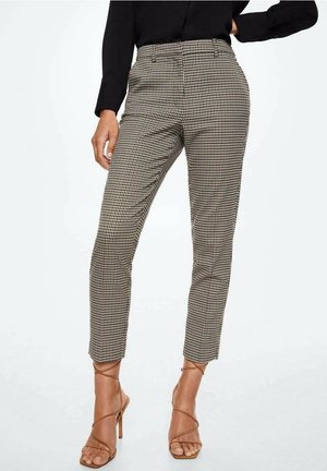 Mujer con top negro, pantalones ajustados hasta el tobillo con estampado de pata de gallo en beige y negro, y sandalias de tacón alto en color marrón claro con tiras en el tobillo.