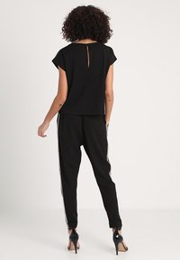 Svart kortärmad topp med nyckelhålsdetalj bak, tillsammans med svarta joggers med vita sidont menyer och blixtlås vid anklarna, bärs med svarta högklackade skor.