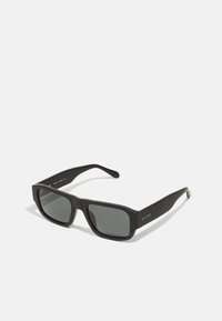 Gafas de sol rectangulares negras con lentes tintados y textura mate. Cuentan con patas anchas y un logo discreto en el lateral.