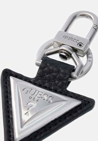 Portachiavi in pelle nera con una piastra metallica triangolare argentata incisa con "GUESS USA" e un gancio metallico per il fissaggio.