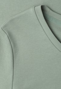 Close-up of soft light green fabric showing the shoulder and V-neck collar stitching details of a garment.