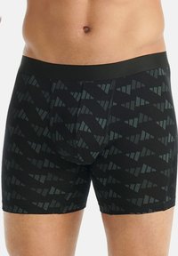 Detailní záběr mužského trupu oblečeného v černých boxerky s geometrickým trojúhelníkovým vzorem a pevným černým pasem.