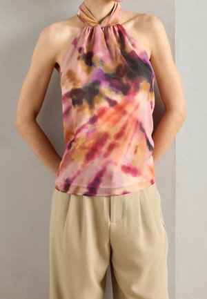 Personne portant un haut sans manches à col noué tie-dye aux teintes rose, orange et marron, associé à un pantalon beige ample.