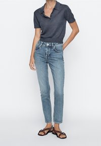 Polo shirt à manches courtes gris foncé, jeans taille haute bleu clair et sandales plates marron avec un détail de boucle décoratif.