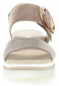 Beige suede sandal with a wide front strap and a back ankle strap. Features a decorative round brown buckle and a chunky white sole.