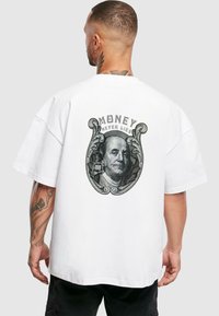 Liela izmēra balta T-kreklu ar grafisku attēlu, kurā redzams Benjamins Franklins un frāze "NAUDA NIKAD NESAKĀ" uz aizmugures. Ikdienišķa kokvilnas auduma.