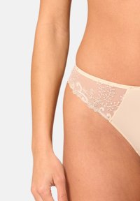 Beige kanten panties met een sheer mesh zijkant, versierd met bloemendoordringing en geschulpte randen, die een delicate en textuurrijke uitstraling geven.