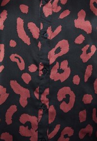 Blusa nera con stampa leopardata rossa. Presenta una texture satinata liscia e bottoni neri lungo la parte anteriore.