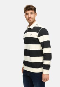 Polo a maniche lunghe a righe verticali nere e crema. Caratterizzato da un colletto, spacco laterale e logo ricamato sul petto. Tessuto in cotone morbido.