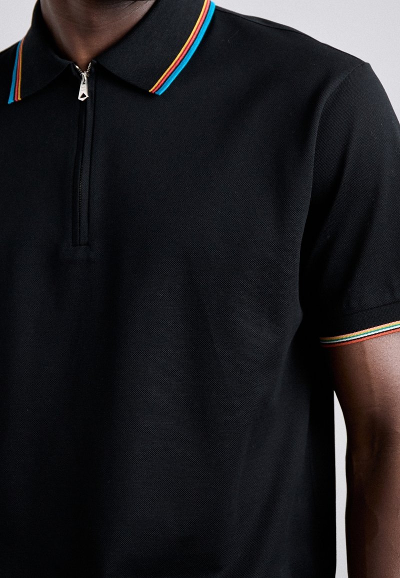 Polo noir à manches courtes avec zip devant, col et bords des manches présentant de fines rayures rouges, jaunes et bleues.