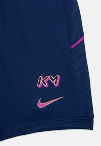 Námornícke modré športové šortky s priedušnou štruktúrou, ružovými akcentmi a zlatými logami: "KM" a Nike swoosh, umiestnenými blízko lemu.