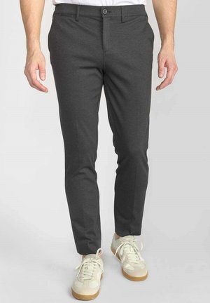 Grijze broek gemaakt van een gladde stof, met een slim fit, voorzien van een knoopsluiting en zijzakken. Gecombineerd met lichtgekleurde sneakers.