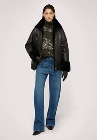 Czarna skórzana kurtka z futrzanym kołnierzem, noszona na ciemnym swetrze w wzory, w połączeniu z jasnoniebieskimi dzwonowatymi jeansami i czarnymi botkami na kostkę.