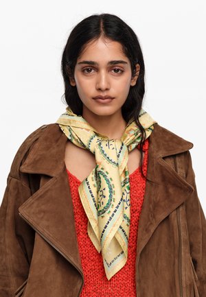 Noor naine tumedate juustega kannab pruuni seemisnahast jopet, punast kootud topi ja kollast mustrilist salli, mis on ümber kaela seotud.