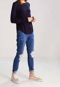 Marineblå långärmad tröja med ribbad struktur, i kombination med ljusblå slitna jeans och beige högskor med rosa detaljer.