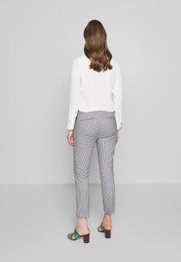 Vit långärmad blus kombinerad med grå rutiga byxor, med slim fit och smalnande ben, kompletterad med svarta och gröna klACKfötter.