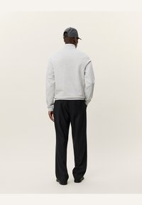 Grå hettegenser med høy krage, brukt sammen med mørke bukser, sett fra baksiden. Enkelt design og vanlig passform, ingen synlige mønstre.