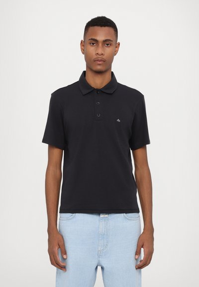 Polo shirt nero in cotone con colletto, apertura a tre bottoni e un piccolo logo sul lato sinistro del petto. Abbinato a jeans in denim blu chiaro.